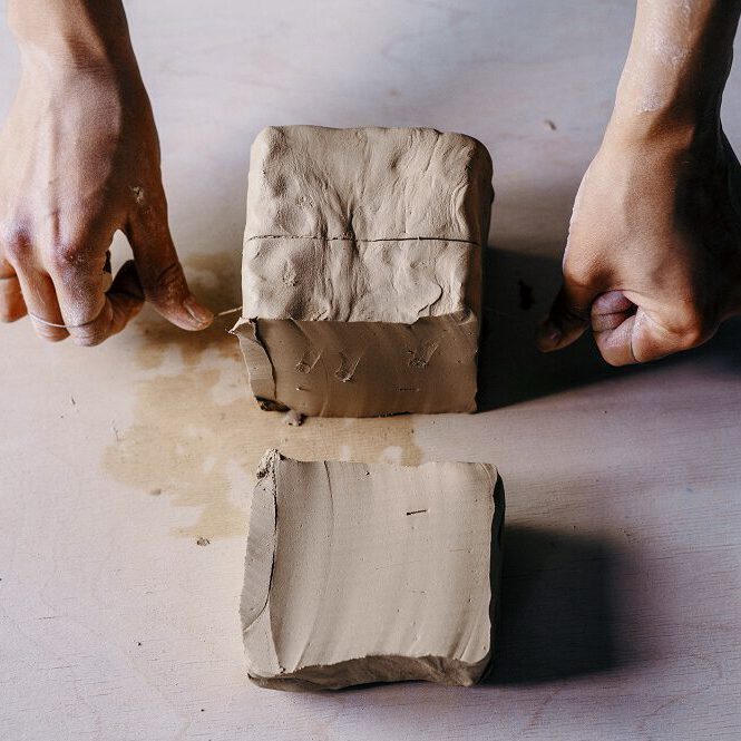 Female potter hands working with clay in workshop. White desk on background